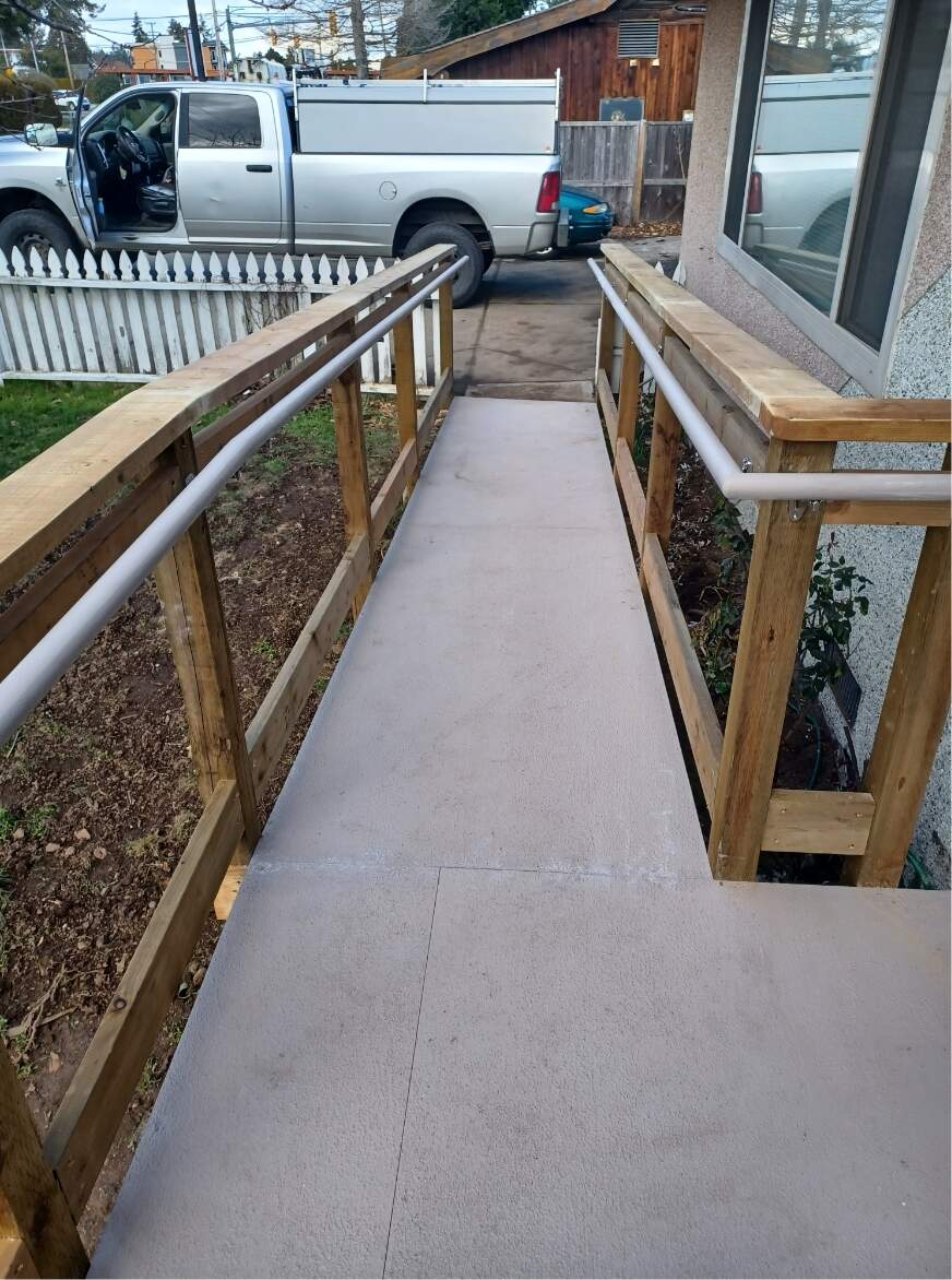 entrance accessibility ramp with wooden sides and handles coming down to driveway with silver truck parked with door open